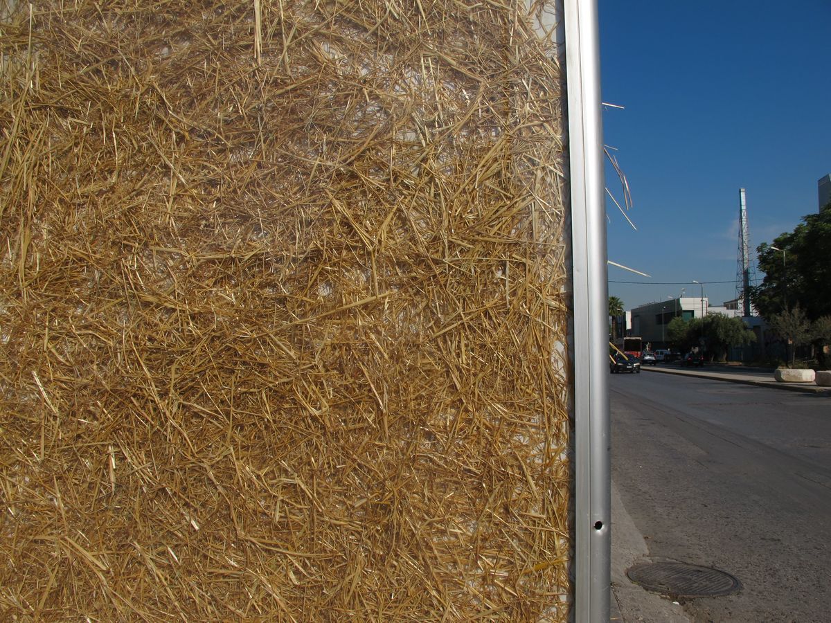 Close-up of straw packed densely behind the glass of an advertising panel, edge of the metal frame against a street view and blue sky.