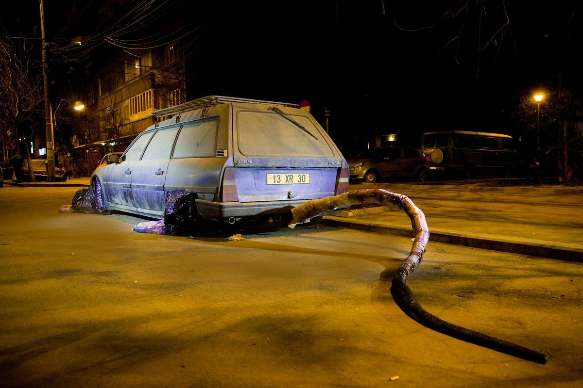 Rear view of the same station wagon at night, its purple tube tail coiling across the pavement toward the camera, parked cars and streetlights behind.