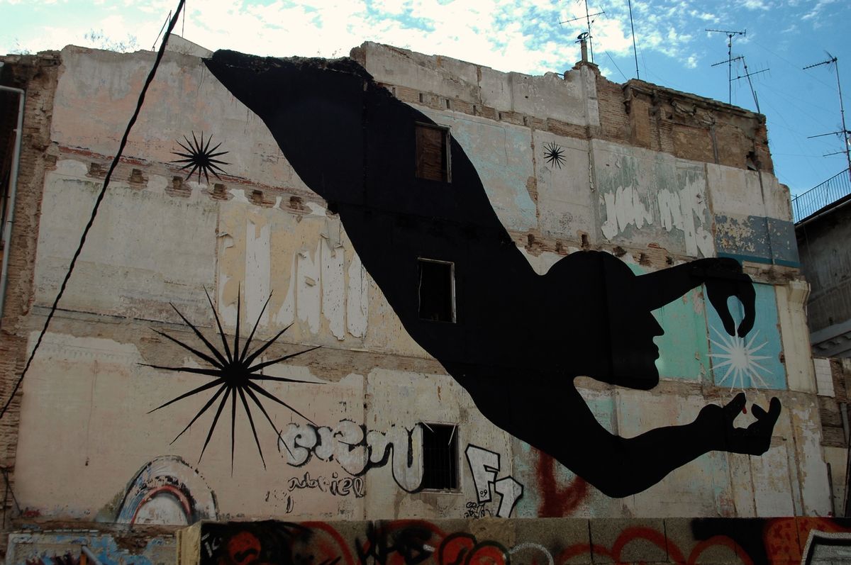 Large black diagonal silhouette of a falling figure with a profile face, arm extended toward a small white star burst, painted across a demolished building facade covered in other star shapes and graffiti.