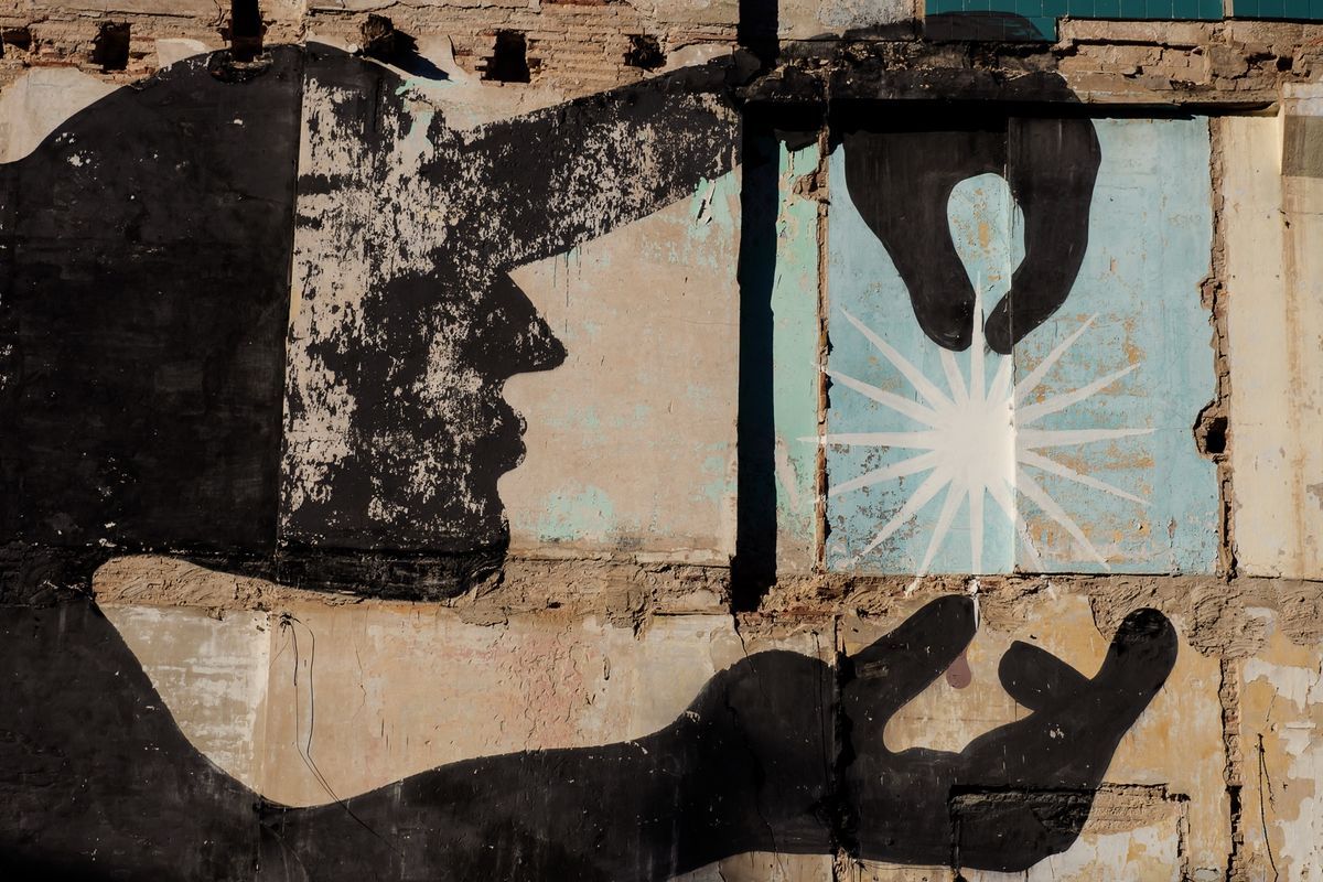 Close-up of the same mural showing the figure's profile face and two open hands, one hand reaching toward a white star burst painted on a teal panel, weathered plaster wall around it.