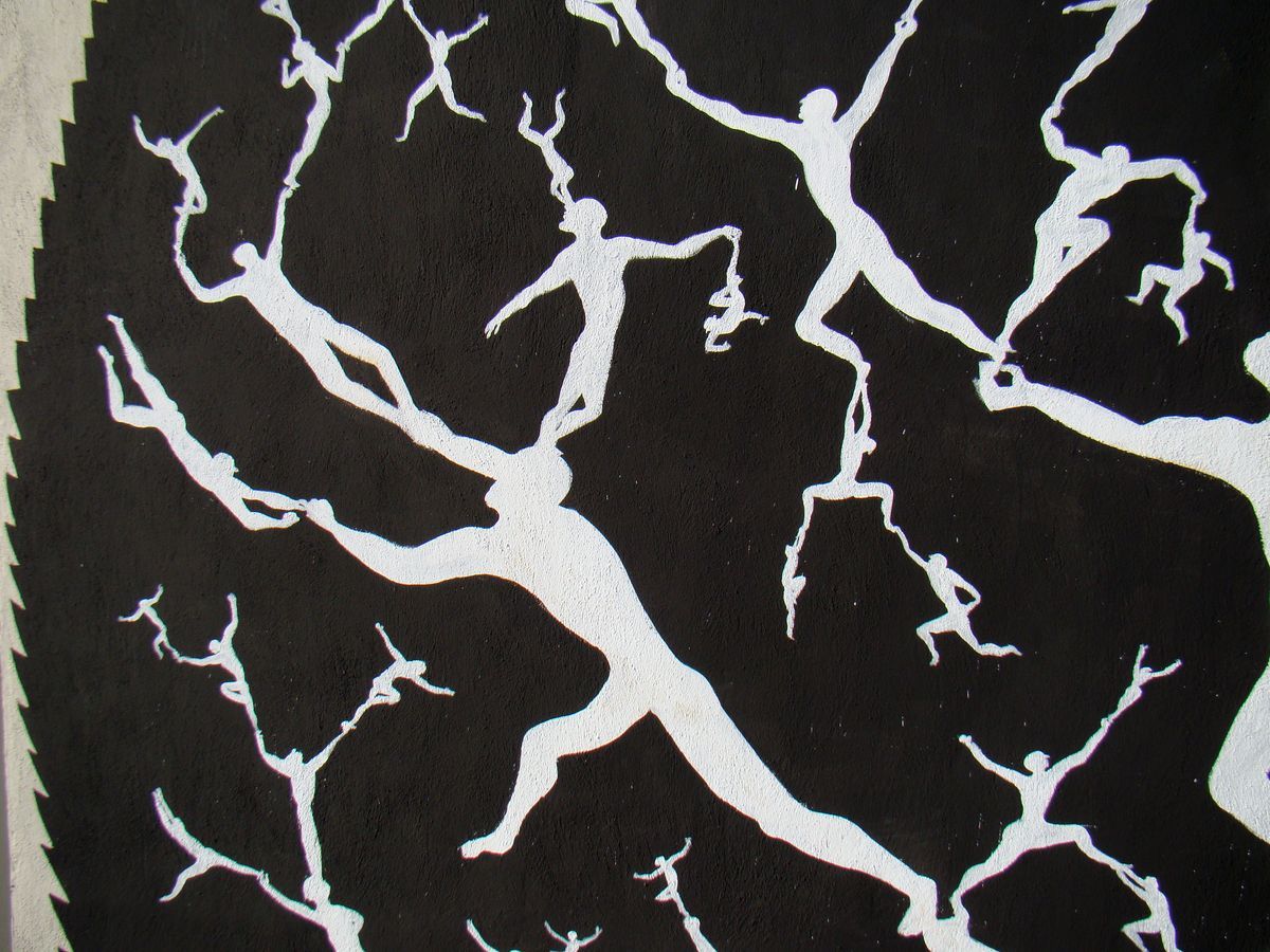 Close-up of a black and white mural showing white branching tree-like limbs full of small dancing human figures perched along the branches, spreading across a dark background.