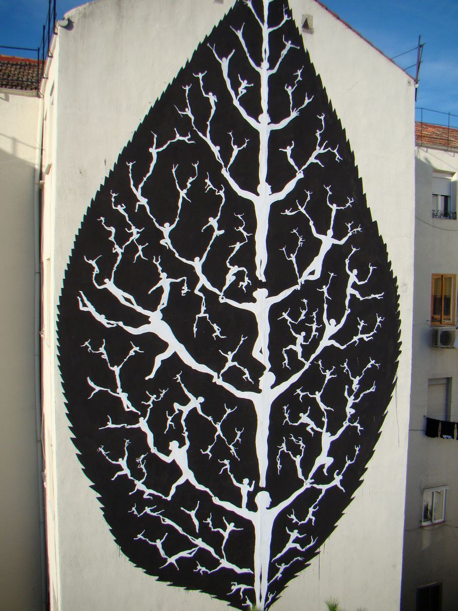 Wide view of the same building gable painted as a giant leaf shape with a white branching vein pattern made of tiny human figures against a black background, apartment windows visible on either side.