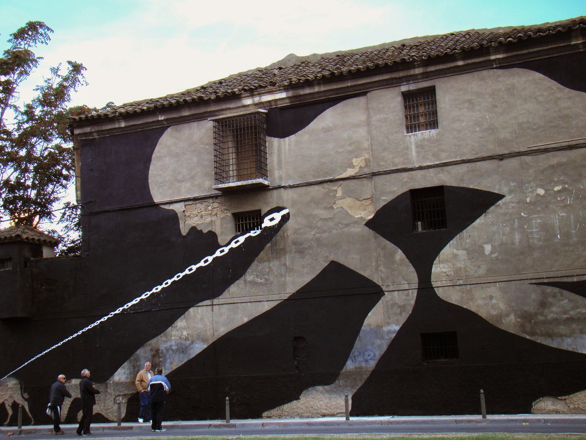 Black silhouette of a bent figure with a long chain leash trailing from its mouth down to a small donkey at the bottom of a building wall, dark negative space forming an hourglass shape between two barred windows, people standing on the street below.