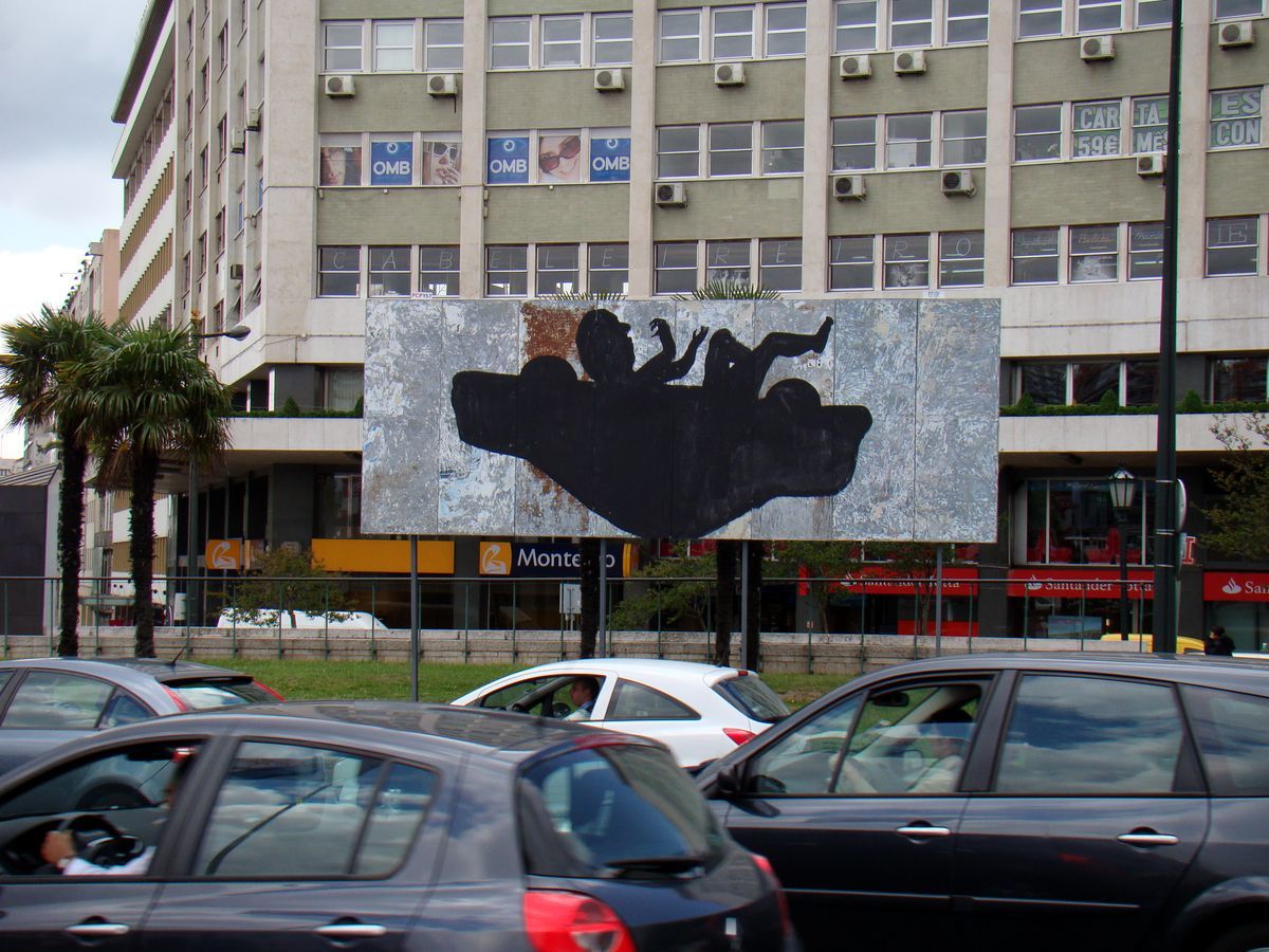 Large billboard on a city rotary painted with a black silhouette resembling an overturned car with wheels and limbs in the air, an office building and passing cars surrounding it.