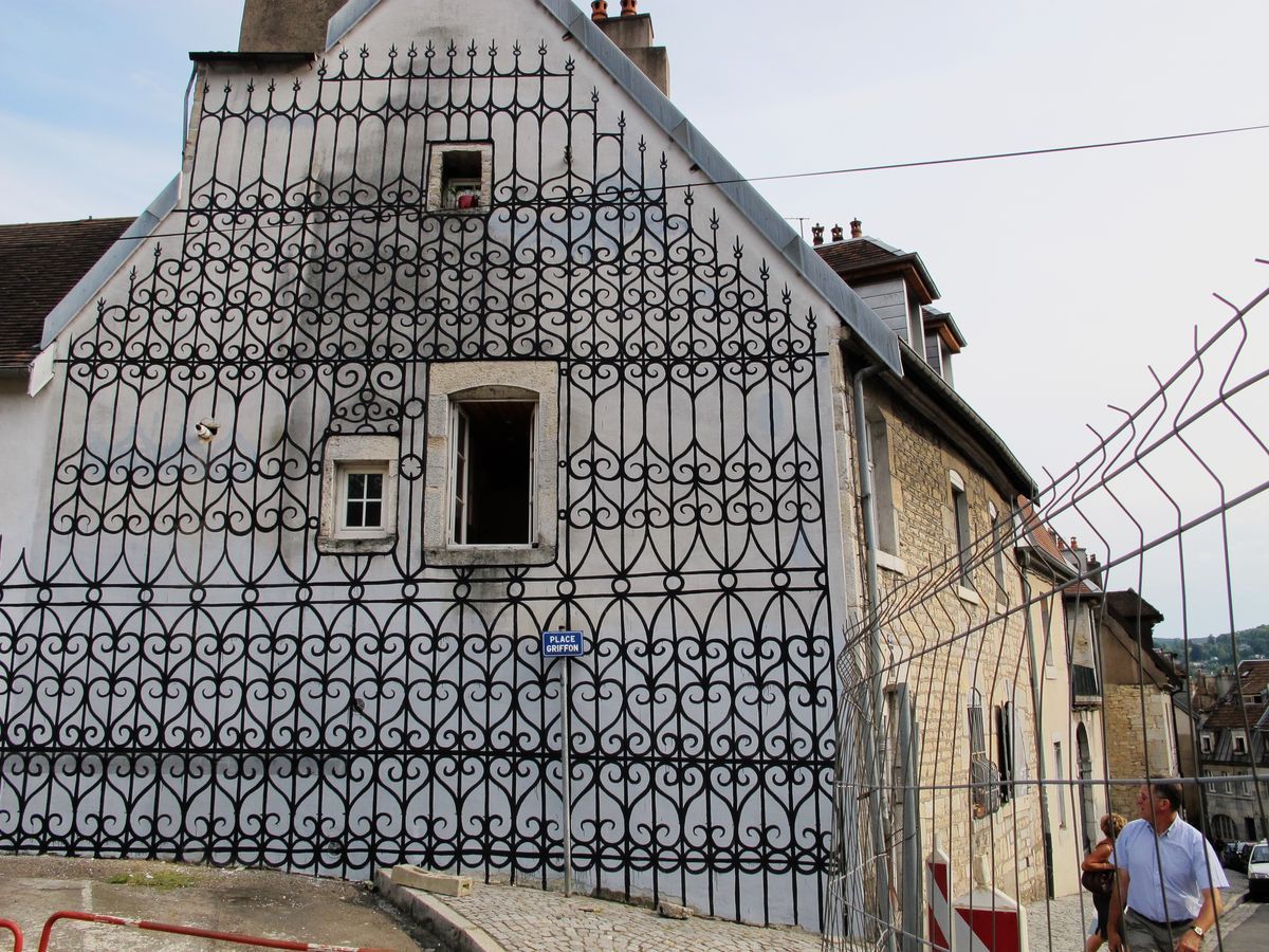 Close-up of the same facade showing the painted wrought-iron grille pattern in detail around a small window and chimney at the roofline.