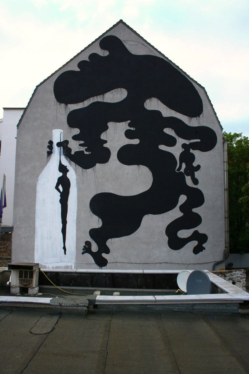 Gable wall painted with a sprawling black cloud-like shape made of soft rounded blobs stretching across the facade, a white silhouette of a genie or spirit figure emerging from a bottle beside it, rooftops and trees in front.