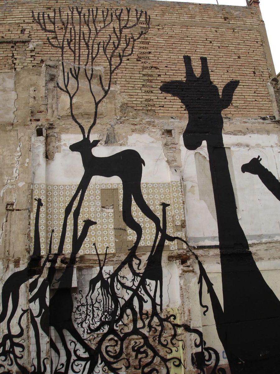 Black wireframe silhouettes of several long-necked giraffe-like animals and a branching antlered deer painted on a weathered brick and tiled building facade, root-like patterns spreading beneath them.
