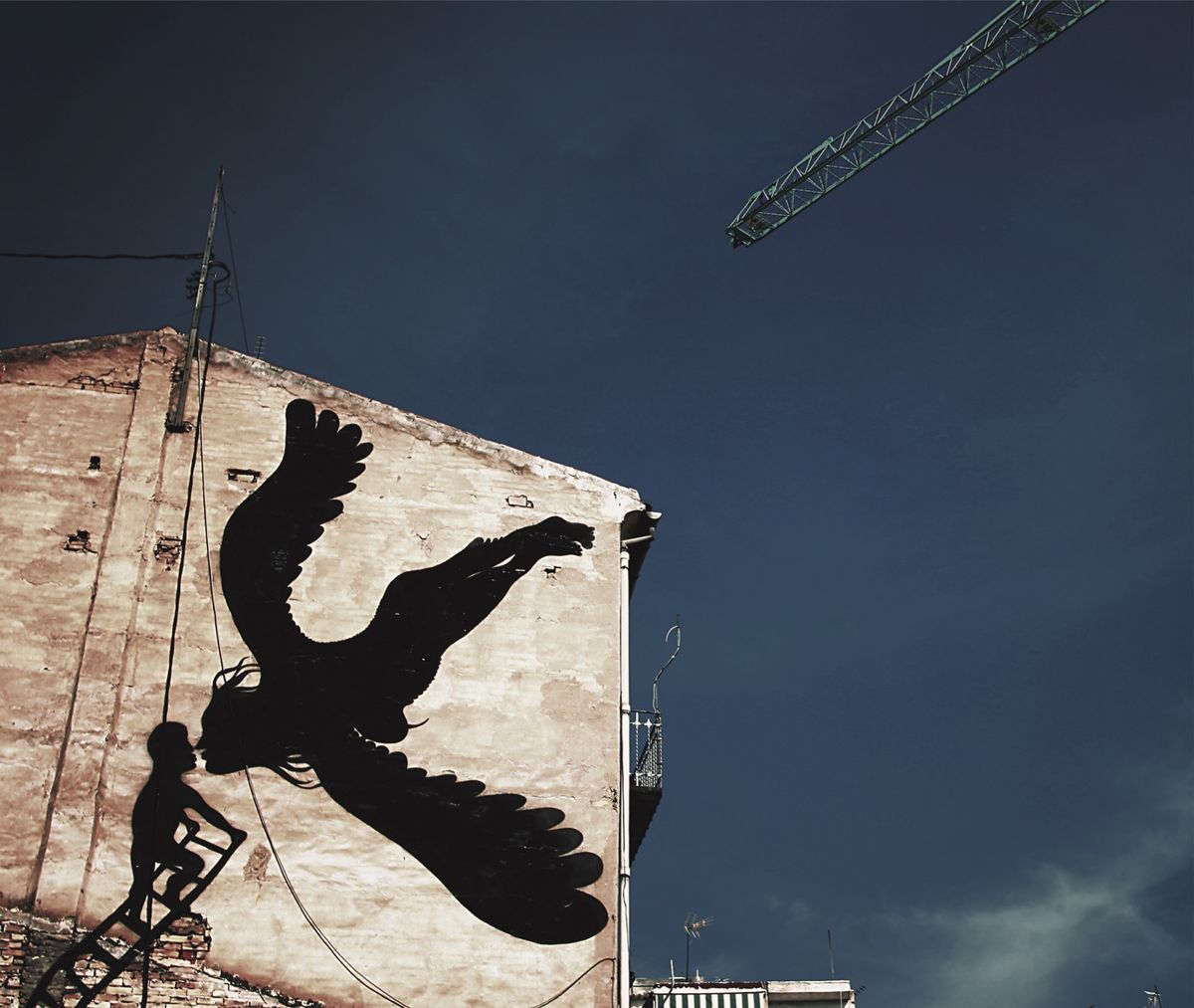 Black silhouette of a large bird in flight with a small child's silhouette climbing a ladder to kiss its beak, painted on a building gable, a construction crane visible in the sky above.