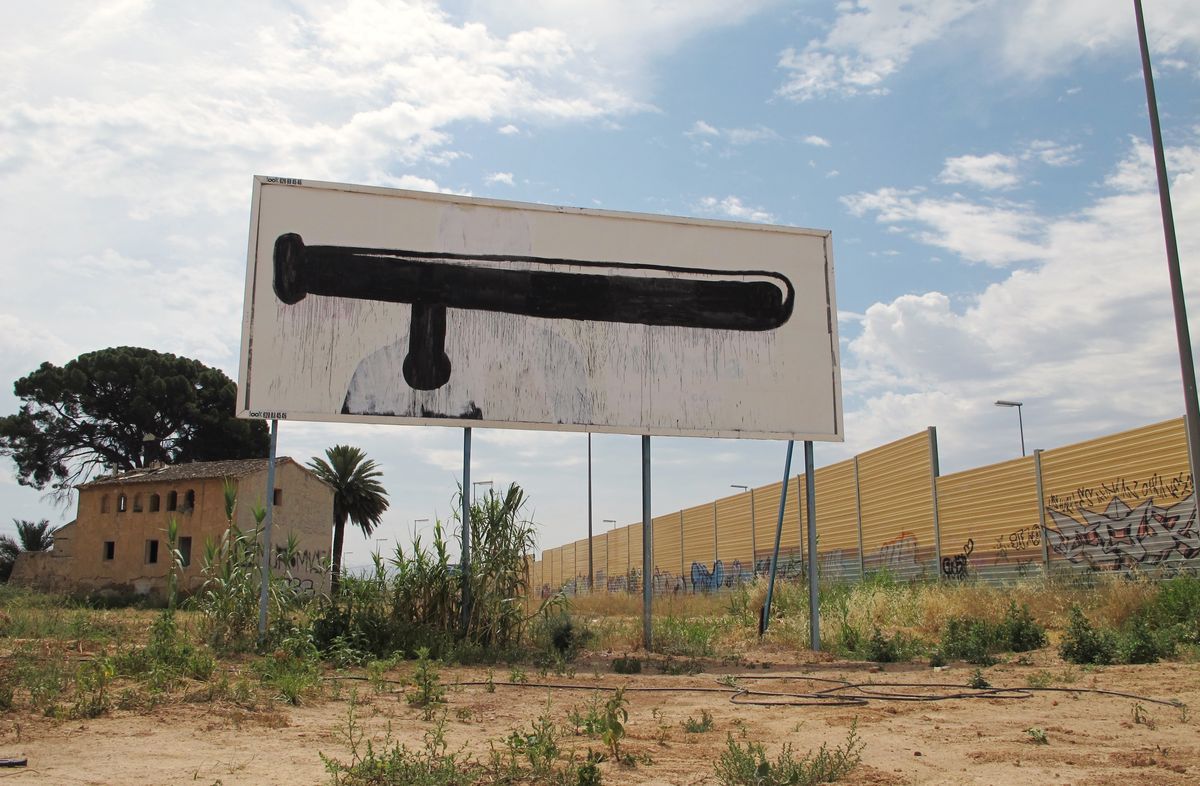 Two roadside billboards side by side, one an advertisement for a clothing shop, the other painted with large black scissors forming a profile face, open grassy field in front.