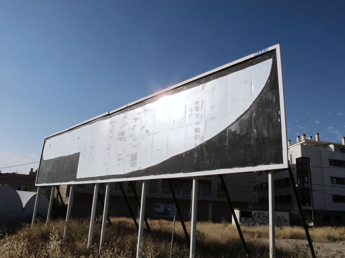 Large roadside billboard backlit by the sun, painted with a black curved diagonal shape sweeping from the top edge down to the bottom left corner, an apartment building visible behind.
