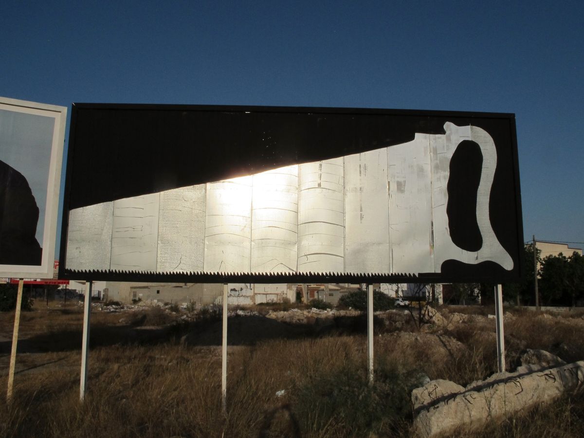 Large black and white billboard shaped like a folding pocket knife, the blade rendered in reflective silver metal with serrated bottom edge, set in a dry field.