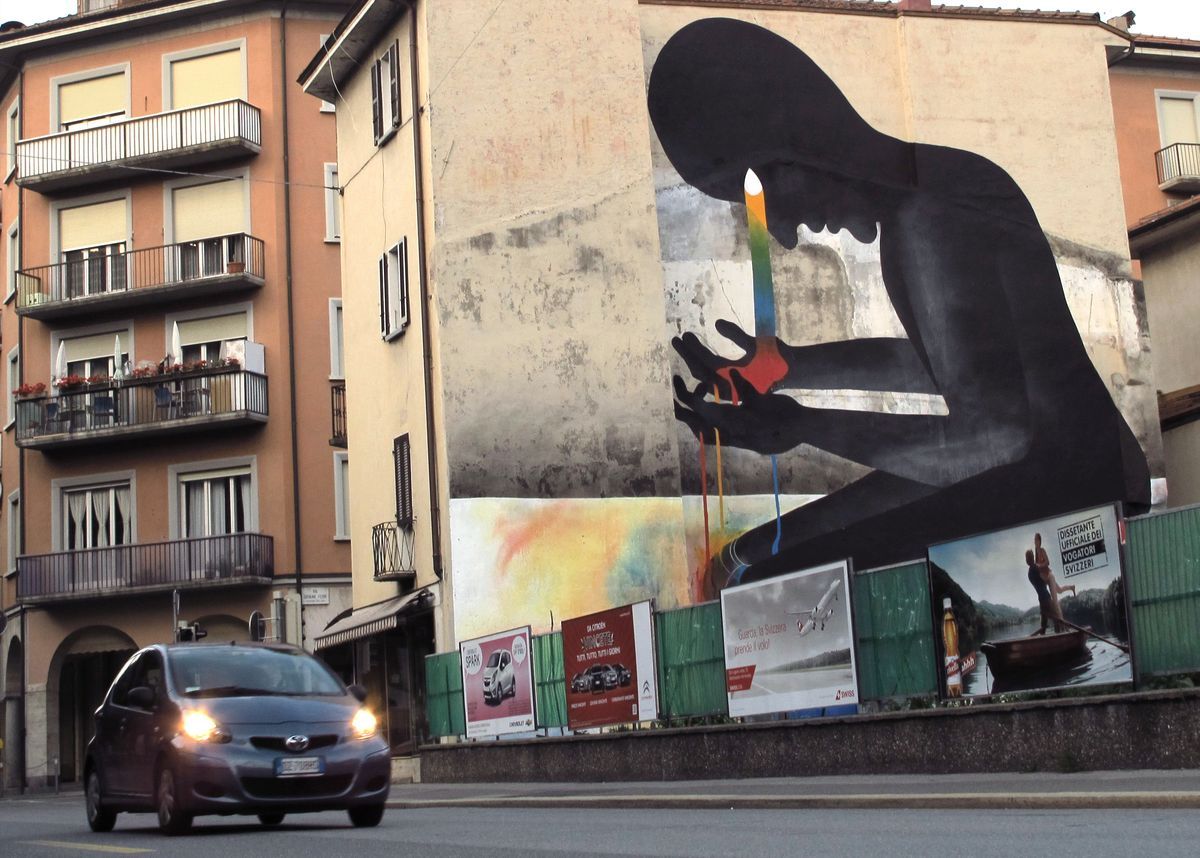 Close-up of the same mural showing the figure's two black hands cupped together, rainbow-colored paint dripping from the fingers down a cracked, weathered wall.