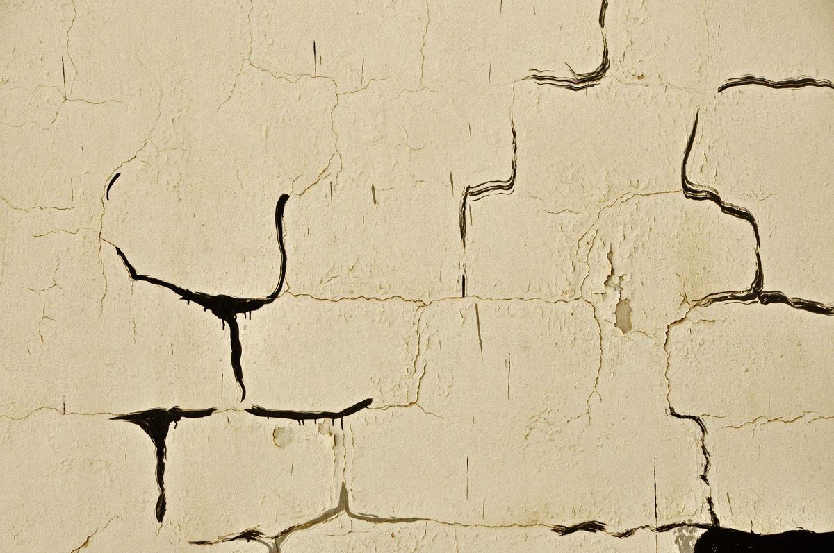 Extreme close-up of the crack mural showing thin black painted lines resembling drips and cracks across a textured cream-colored wall.