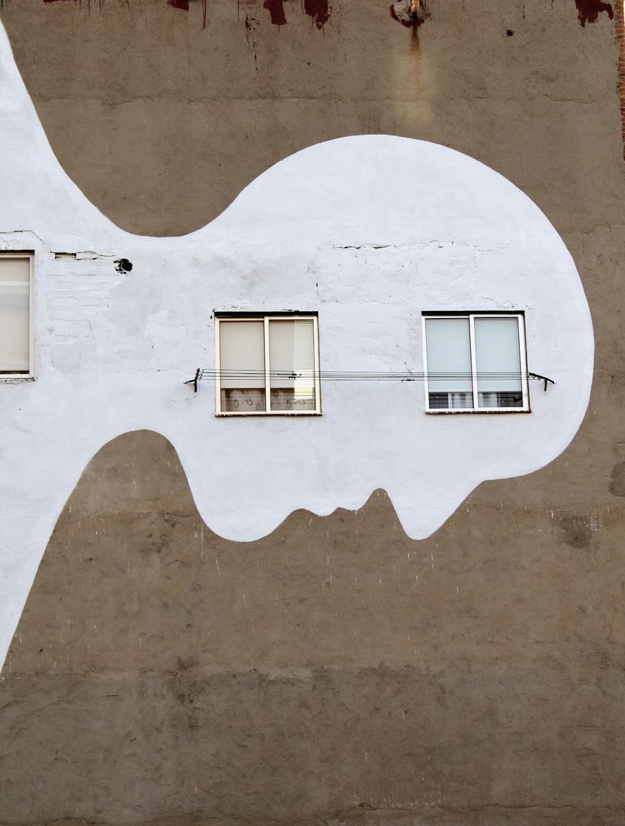 White key-shaped silhouette mural painted on a weathered wall, its rounded head aligned with two windows positioned like eyes.