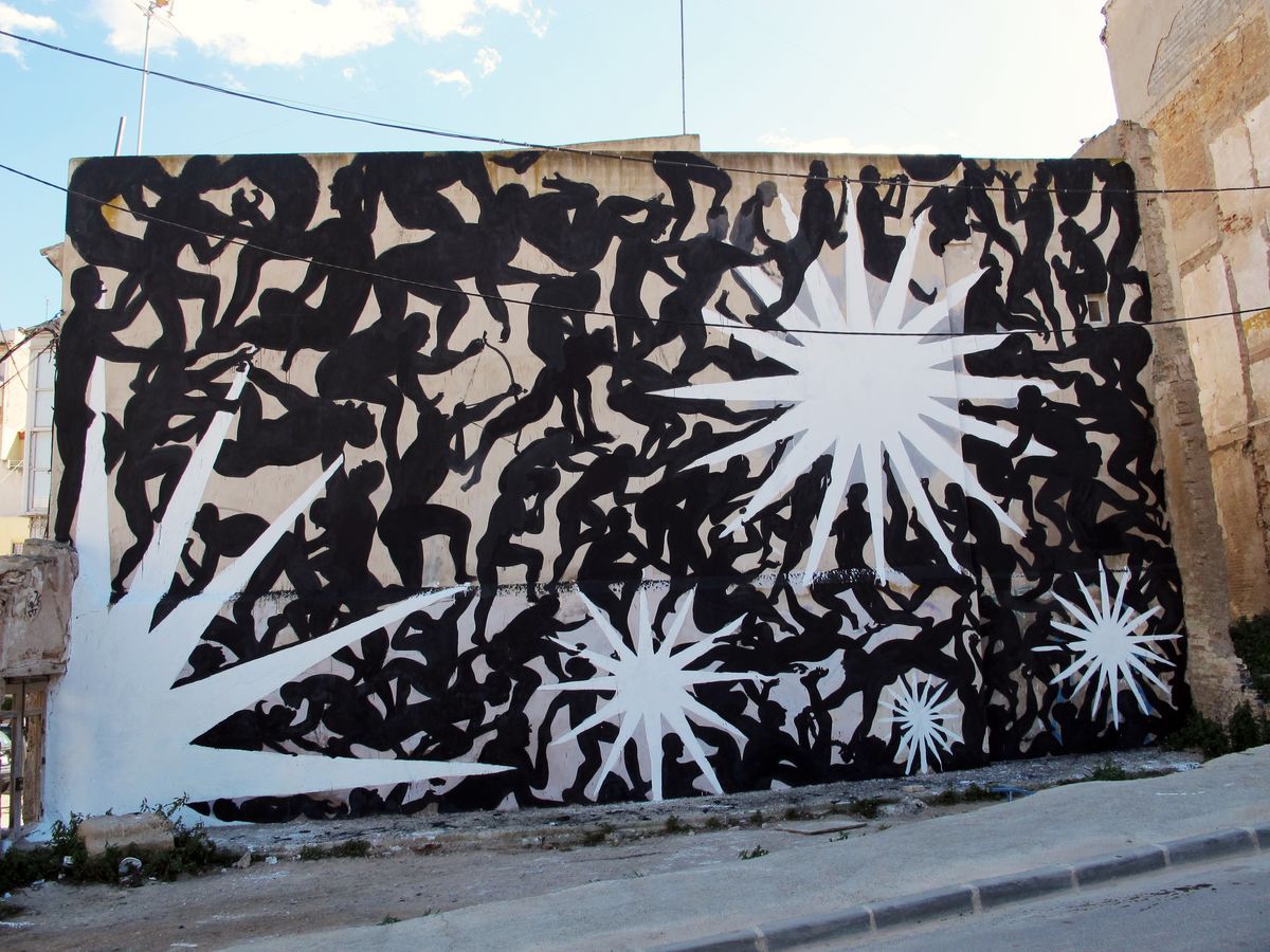 Dense black silhouette mural covering a building wall with dozens of overlapping human figures in various poses, several white multi-pointed starburst shapes radiating across the composition, seen from a street corner.