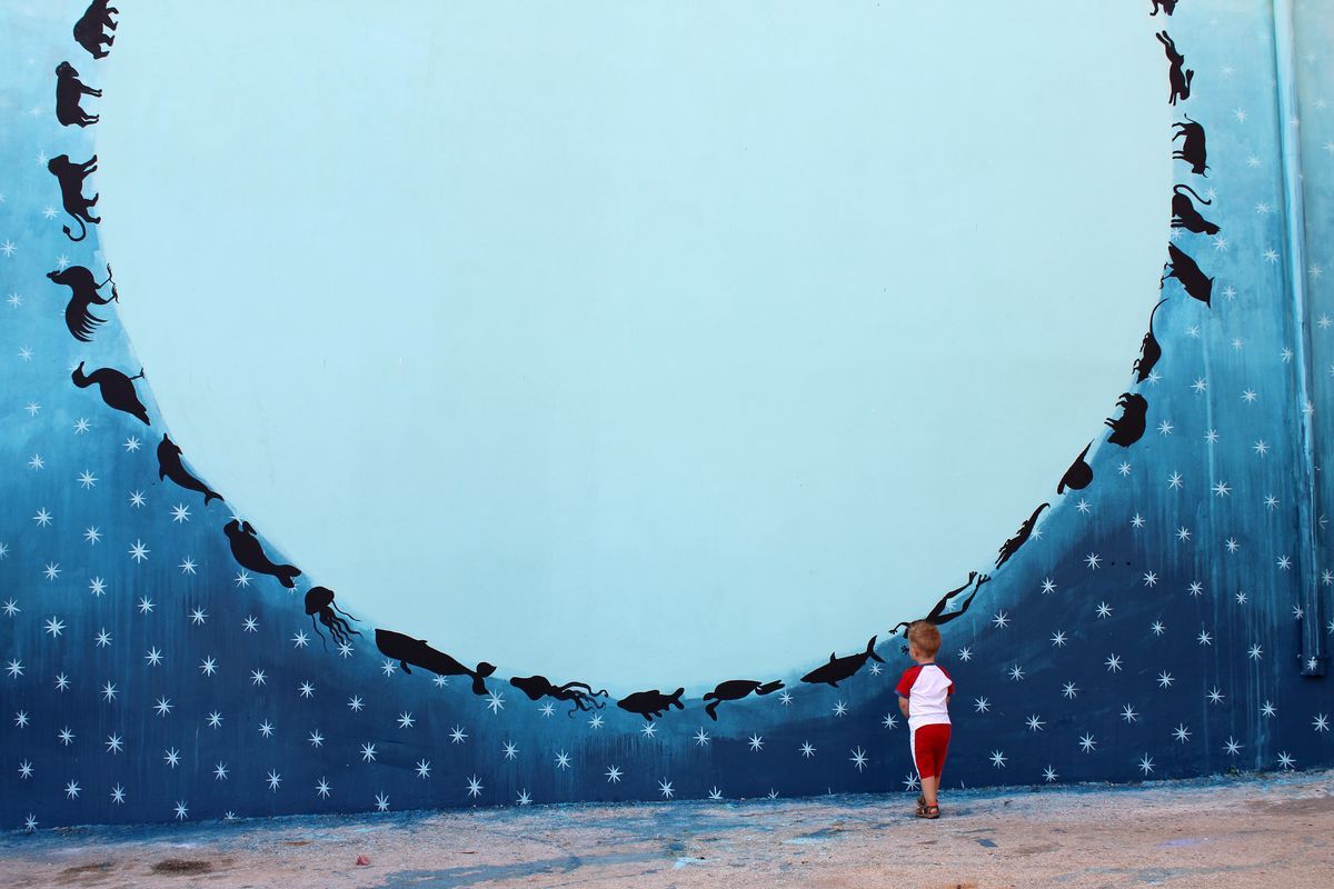 Close-up of the lower section of the circle mural showing sea creatures including a whale, jellyfish, and fish, a small child standing and looking up at the wall.