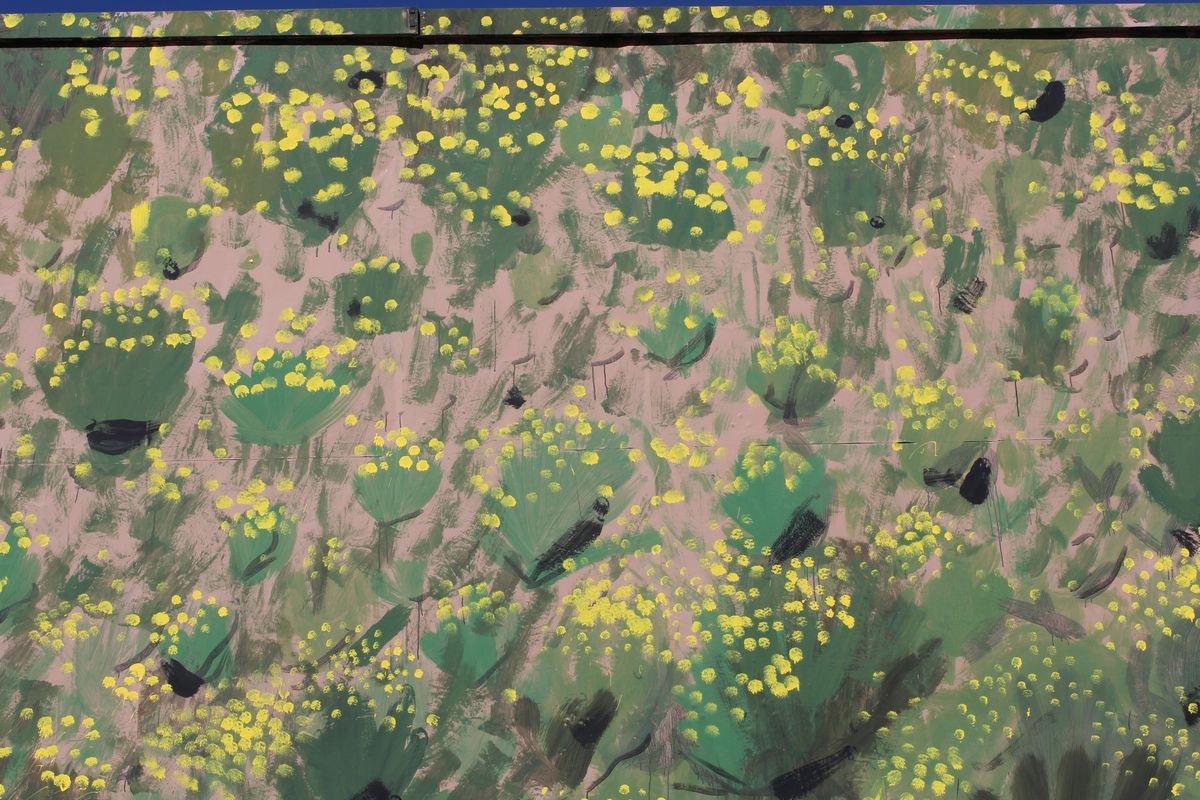 Close-up detail of a billboard painted as camouflage, showing green and dark brushstrokes mixed with clusters of small yellow flowers over a pink-tan ground.