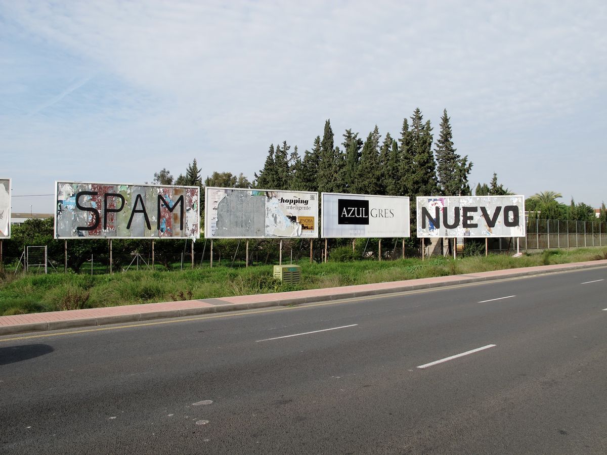Row of four roadside billboards along a street, their surfaces stripped and painted with single black words reading 'SPAM,' a torn poster, 'AZUL GRES,' and 'NUEVO.'