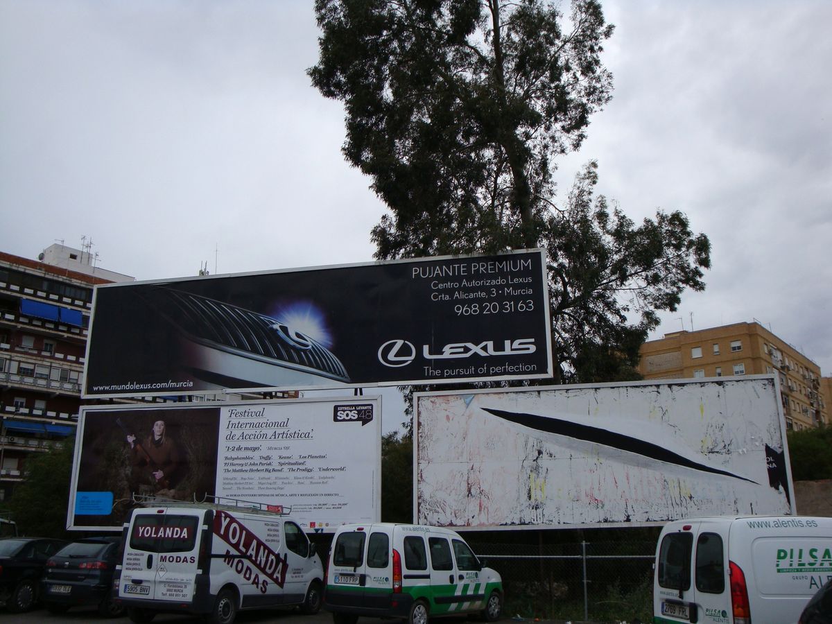 Row of advertising billboards beside a road, the lower right panel painted with a single diagonal black slash cutting across an otherwise blank white surface, echoing Lucio Fontana's slashed canvases, delivery vans parked below.