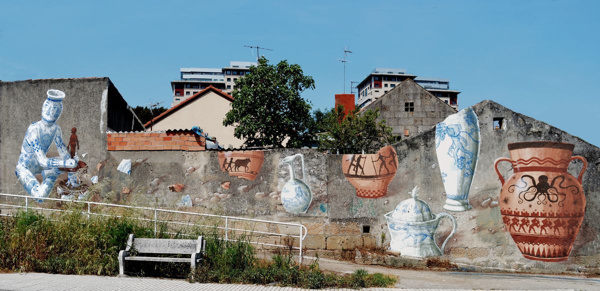 Wide view of a mural on a ruined stone wall showing a full set of oversized painted ceramic vessels: a blue-and-white seated potter figure, several blue-and-white jugs, a terracotta amphora with marching silhouettes, and an amphora decorated with an octopus, city buildings visible behind the wall.