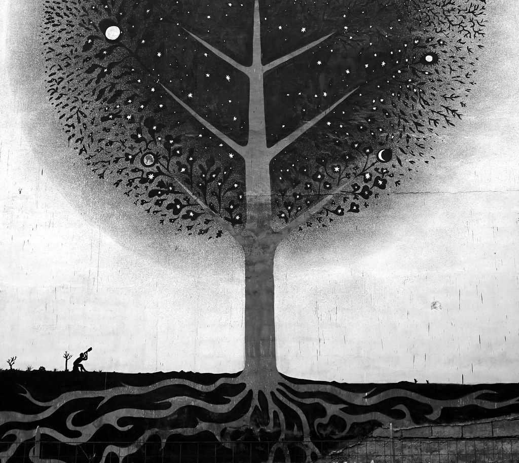 Detail of the tree's starry black canopy with scattered moons and flowers, two tiny silhouetted figures visible on the ground near the roots looking up through a telescope.
