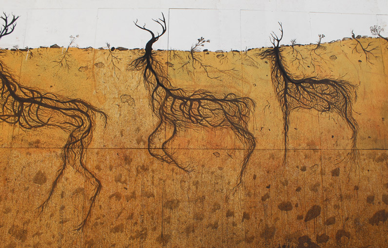 Close-up of three black wireframe deer formed from tangled root lines, one partially cropped, walking across a textured ochre wall beneath a plain white sky band.