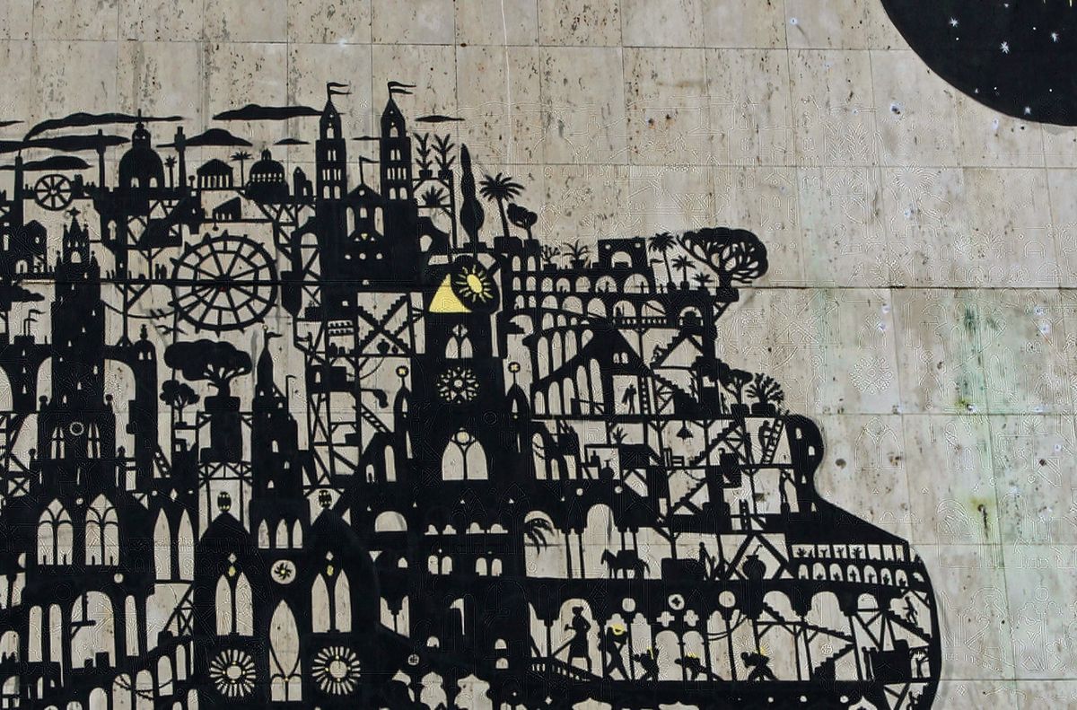 Detail of the black silhouette head formed from an elaborate stacked cityscape of towers, domes, and archways, a few elements picked out in yellow, with the black moon-and-sun circle in the upper corner.