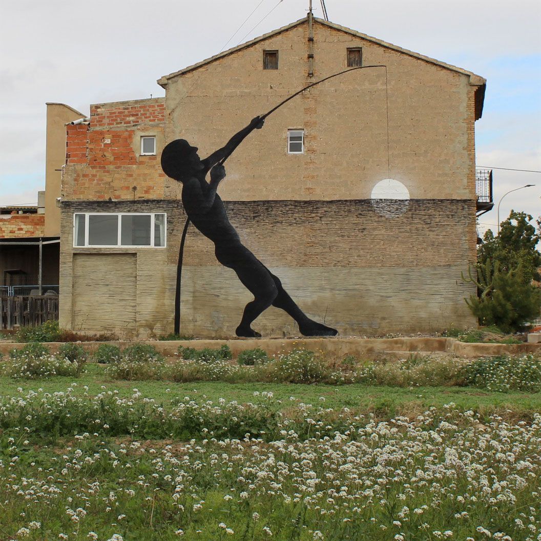 Black silhouette of a fisherman casting a long fishing rod, painted across the upper half of a farmhouse facade above a horizontal band suggesting water with a white sun or moon, set behind a field of white wildflowers.