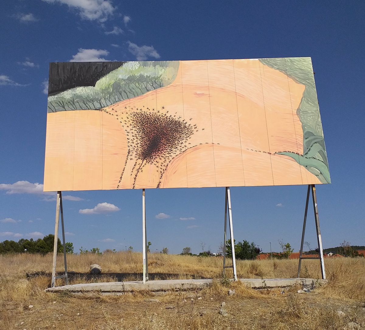 Advertising billboard painted as a homage to Gustave Courbet's L'Origine du monde, its skin-toned surface covered by a dense swarm of black ants converging toward a central mass and trailing off toward green fabric folds at both edges, mounted on metal legs in a dry field.