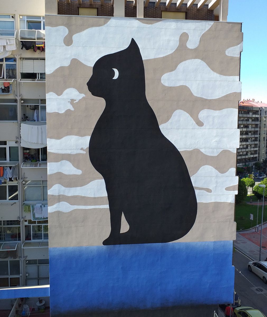 Black silhouette of a seated cat with a crescent-moon eye, painted on the side of a tall apartment building against a camouflage-cloud pattern, above a solid blue lower section.