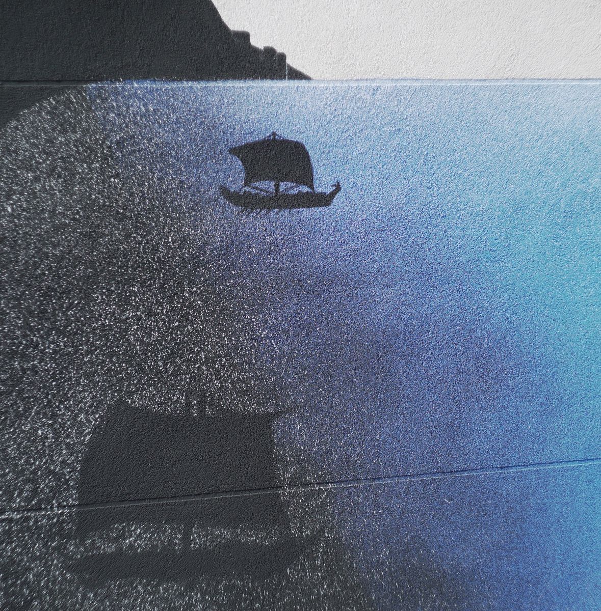 Close detail of a mural showing a small black silhouette sailing ship on a blue gradient sea, its faint reflection visible below, a dark cliff edge in the upper corner.