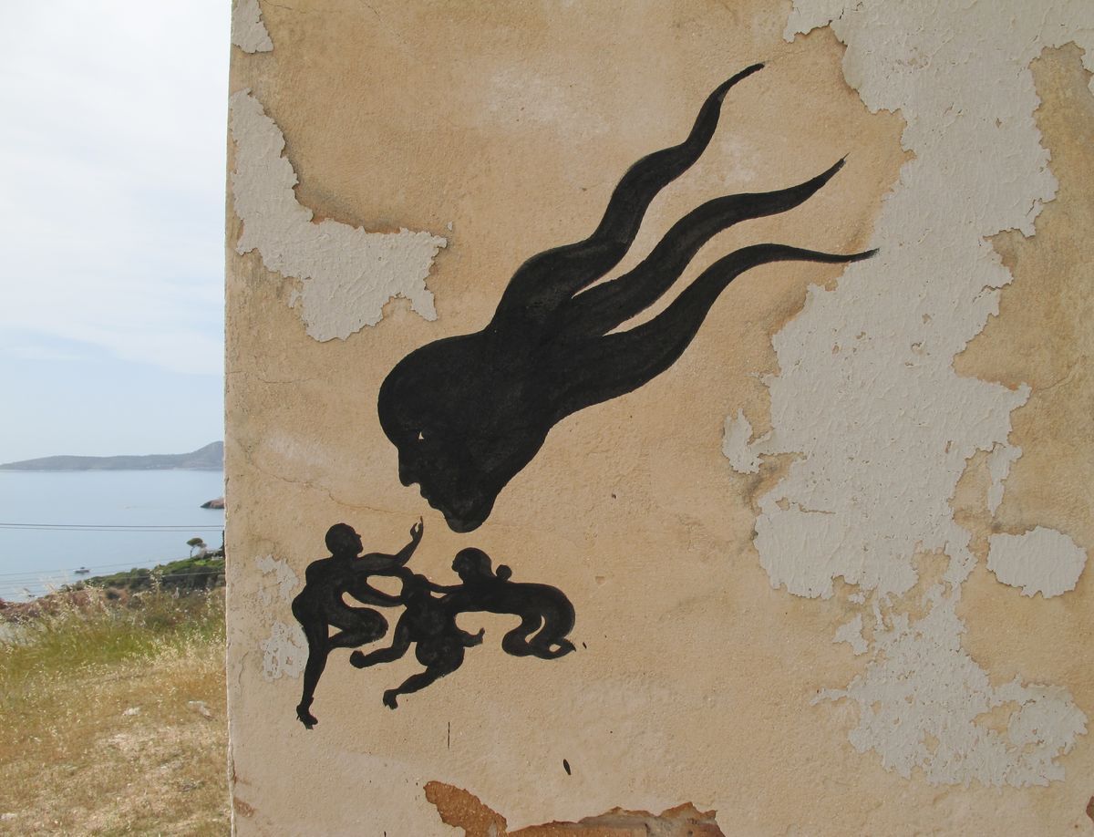 Black mural of a flowing, hair-like female profile trailing off into wavy streaks, with three small silhouetted children reaching up toward her below, painted on a peeling wall overlooking a coastal bay.