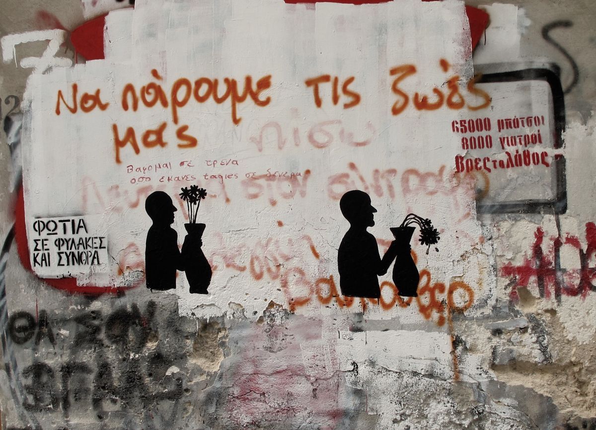 Two black silhouette figures facing each other, each holding a vase of wilting flowers, painted on a wall covered in red spray-painted Greek text and torn white posters.