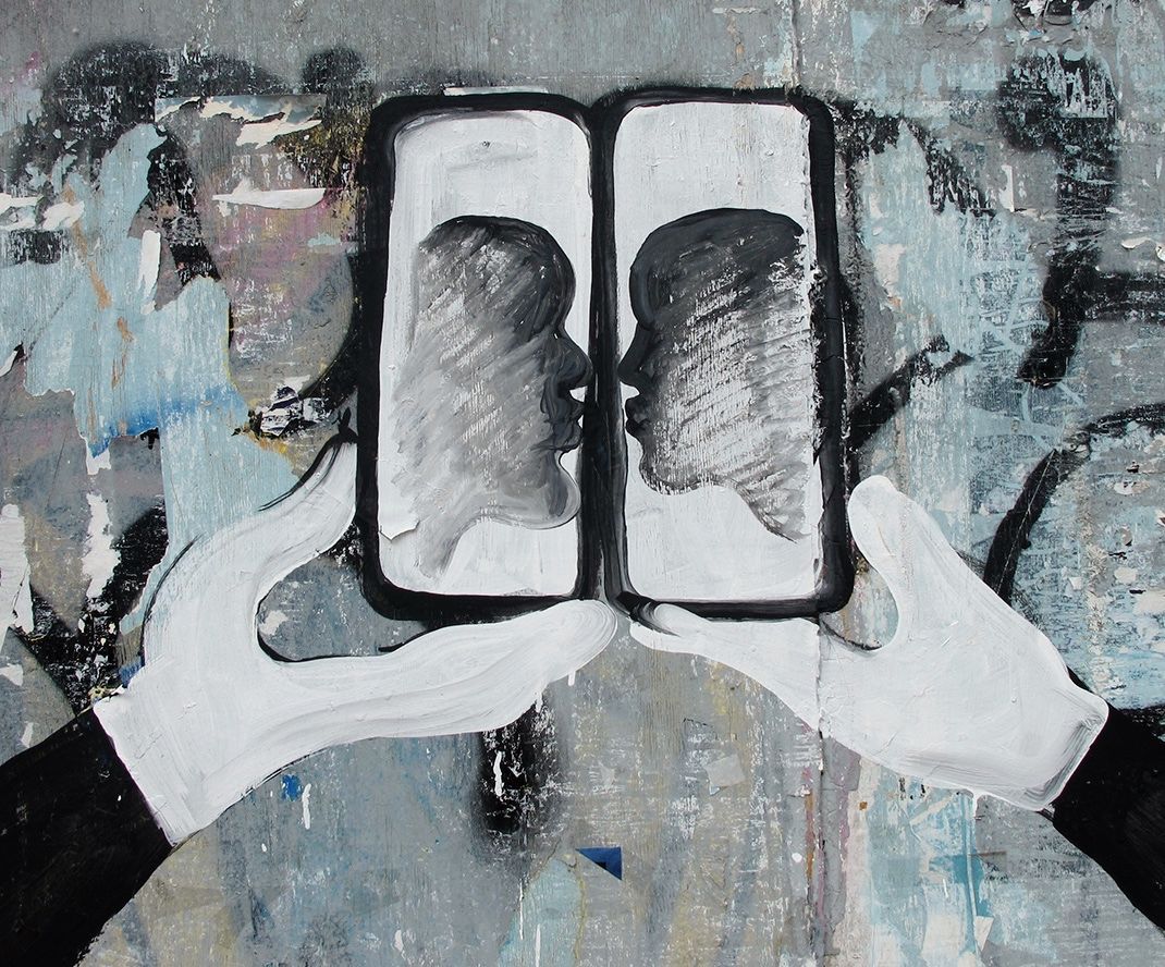 Close-up detail of a black and white mural showing two joined phone screens with silhouetted profiles kissing inside them, framed by two white-gloved hands.