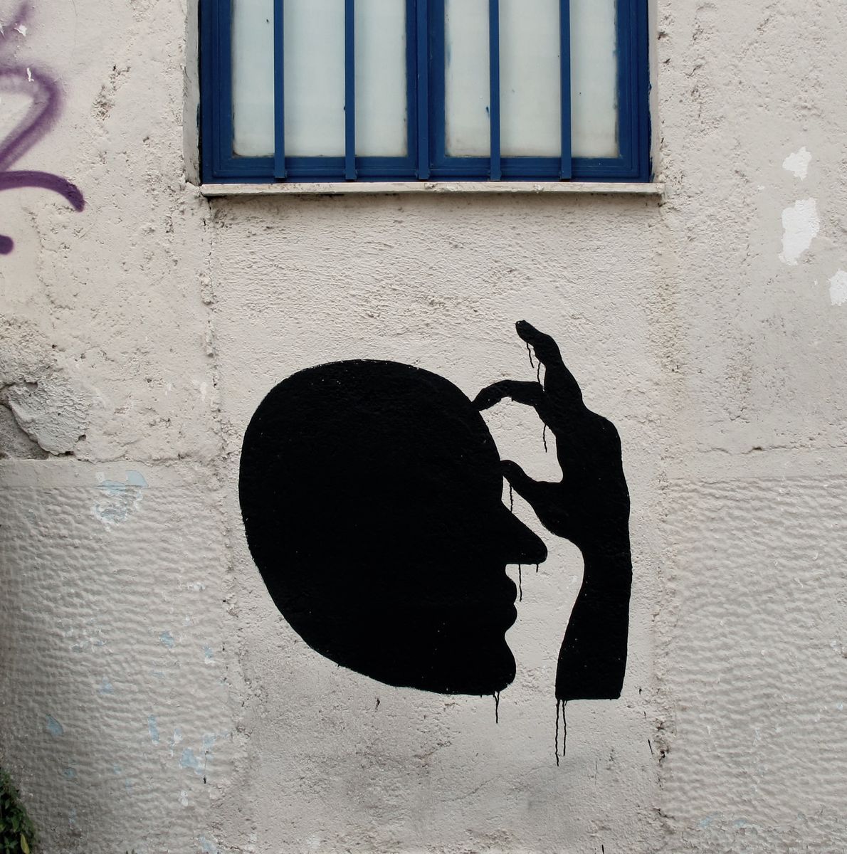 Black silhouette of a head in profile with a dripping hand pressed against its temple, painted on a plain plastered wall beneath a barred window.
