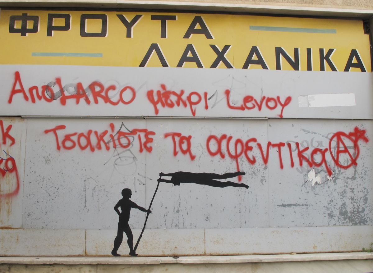 Black silhouette mural of a standing figure using a long pole to lift a horizontal human body, painted on a metal shutter below red spray-painted graffiti text.