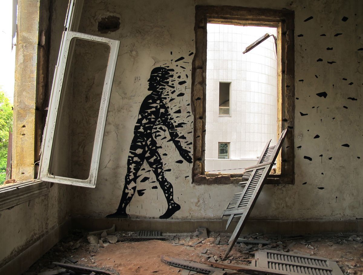 Black silhouette mural of a walking human figure disintegrating into scattered angular fragments, painted on the interior wall of a blast-damaged room with broken window frames and debris strewn across the floor.