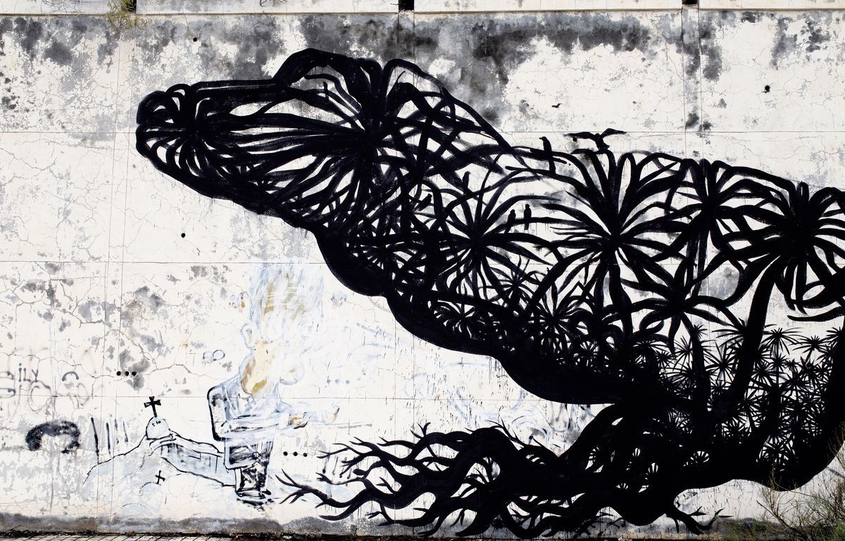 Close-up detail of the black silhouette lizard mural, showing its head and upper body composed of dense, radiating leaf and flower patterns, with faint chalk graffiti visible on the wall beneath.