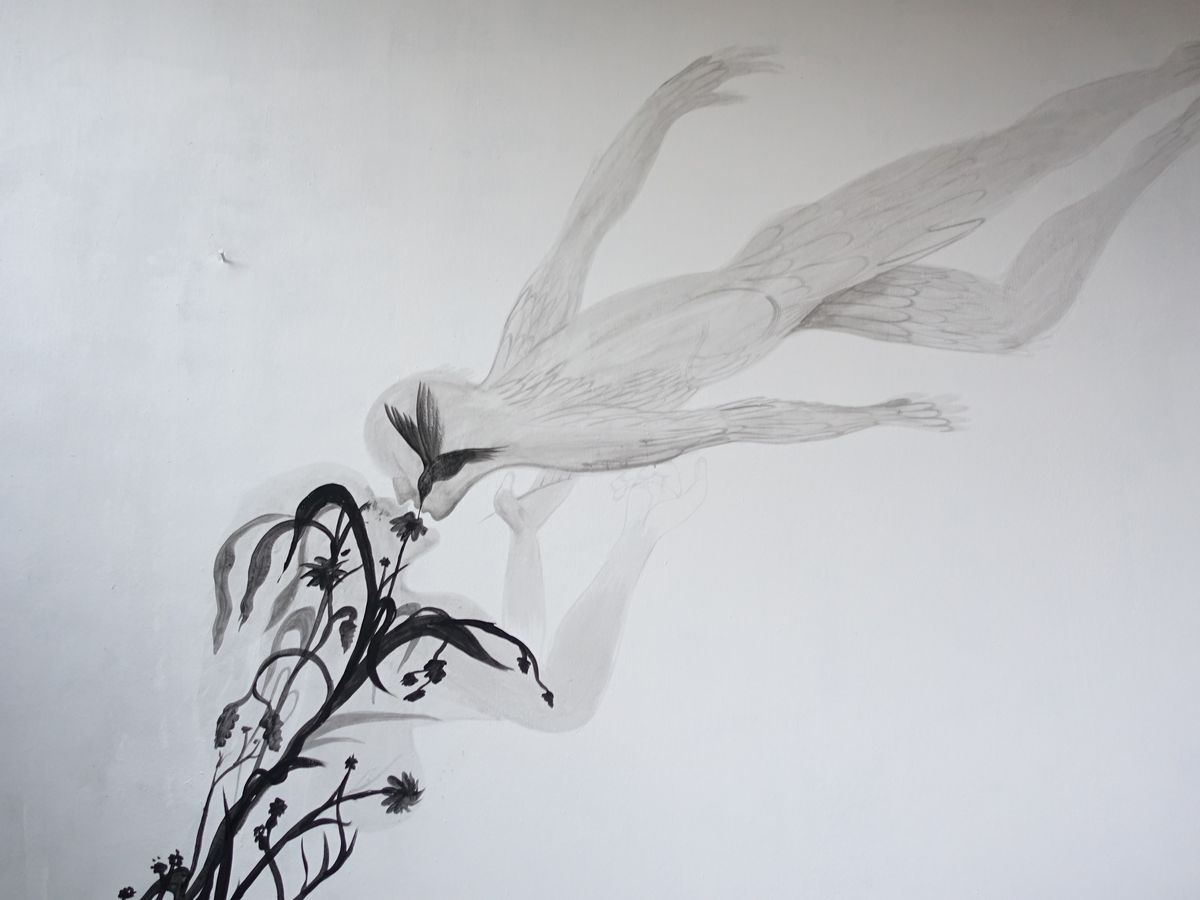 Pale grey mural of a diving bird with outstretched wings above a black flowering branch, painted on a white wall, wide view.