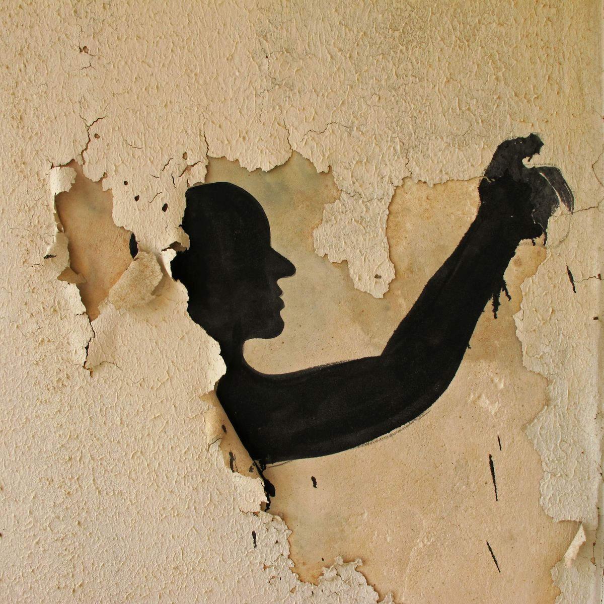 Black silhouette mural of a human head and raised, contorted arm painted on a wall with heavily peeling plaster, the cracked surface exposing patches of bare wall beneath.