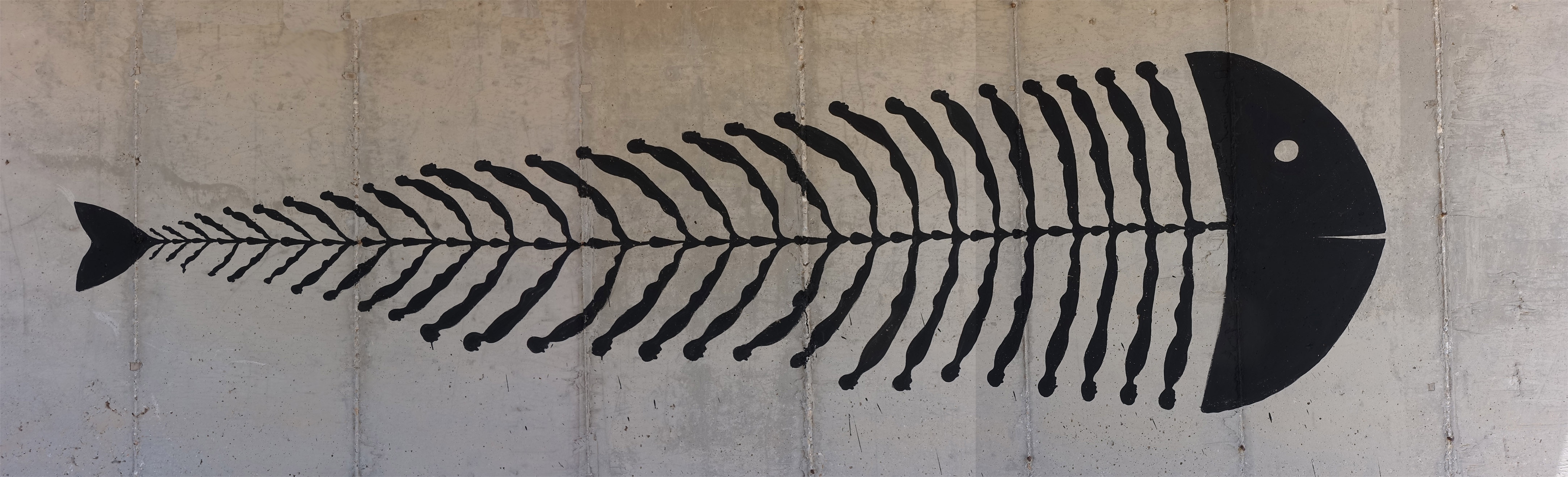 Black silhouette mural of a fish skeleton made from a row of small human figures forming the spine and ribs, painted on a bare concrete wall.