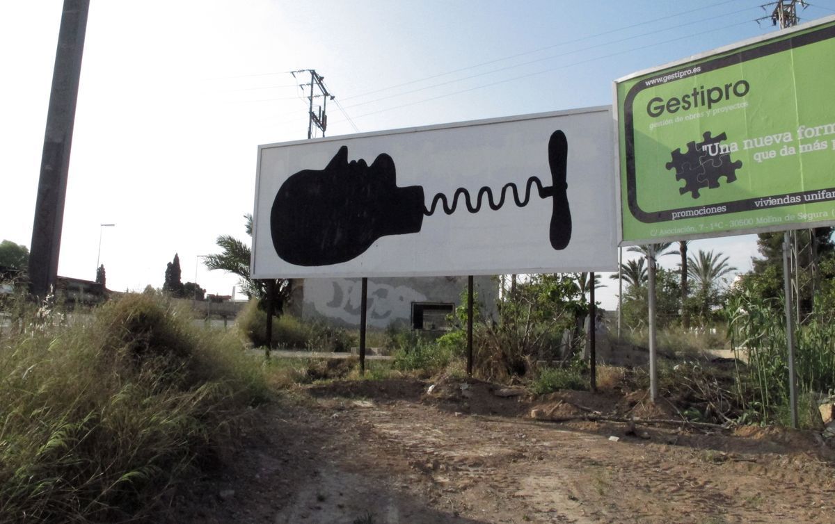 Black silhouette on a roadside billboard showing a bottle-shaped profile head with a corkscrew-like zigzag neck ending in a propeller shape, an unrelated green advertisement panel beside it.