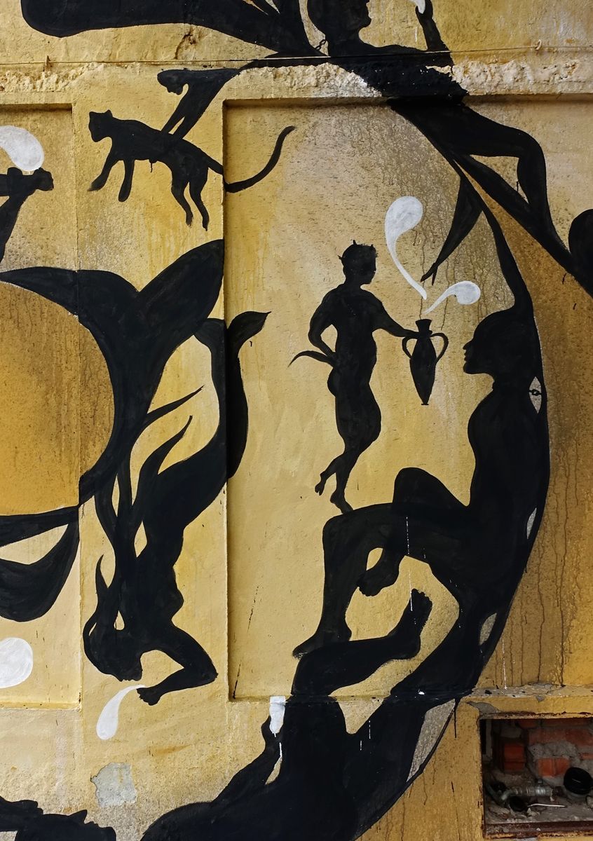 Detail of the snake mural's coiled body filled with black silhouettes of a running cat, a mythological centaur-like figure pouring a jug, and a reclining figure, white splash shapes accenting the yellow background.