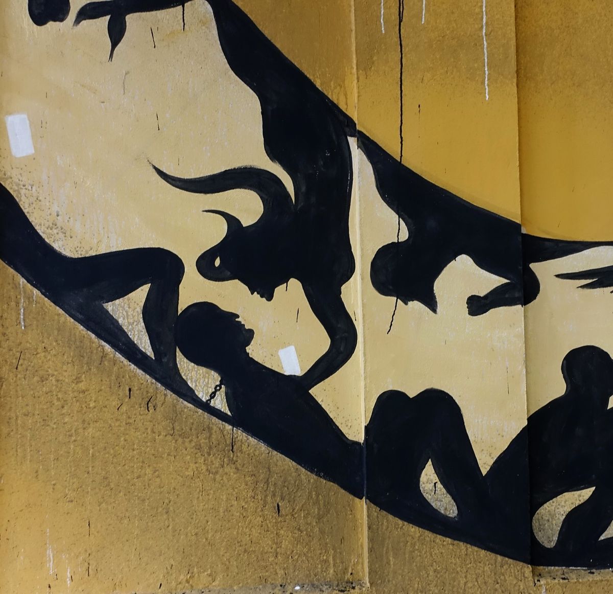 Detail of the snake's body showing a black silhouetted bull-headed minotaur figure, a chained kneeling figure, and other intertwined human silhouettes against the yellow wall.