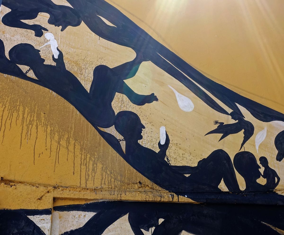 Detail of the snake mural's curving band packed with chained figures, a bird in flight, small child silhouettes, and white teardrop shapes.