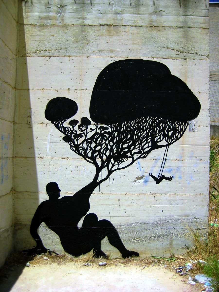 Black silhouette of a hand-cranked wall-mounted phone with a spiral cord stretching to a propeller shape, painted on a white roadside billboard beside an advertising sign for a housing project.