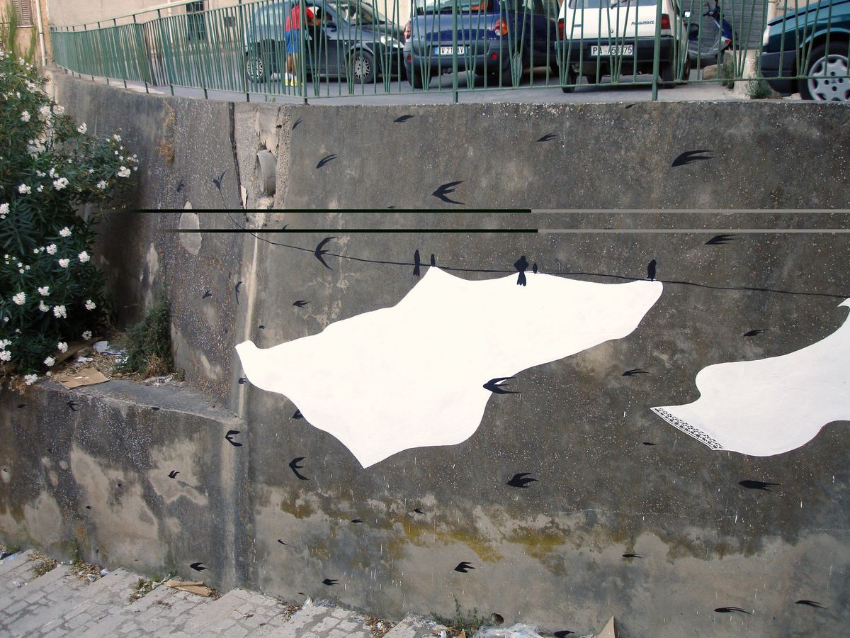Close-up of a single white sheet shape clipped to the clothesline against a weathered concrete wall, small black swallow silhouettes scattered around it, a drainage pipe opening above.