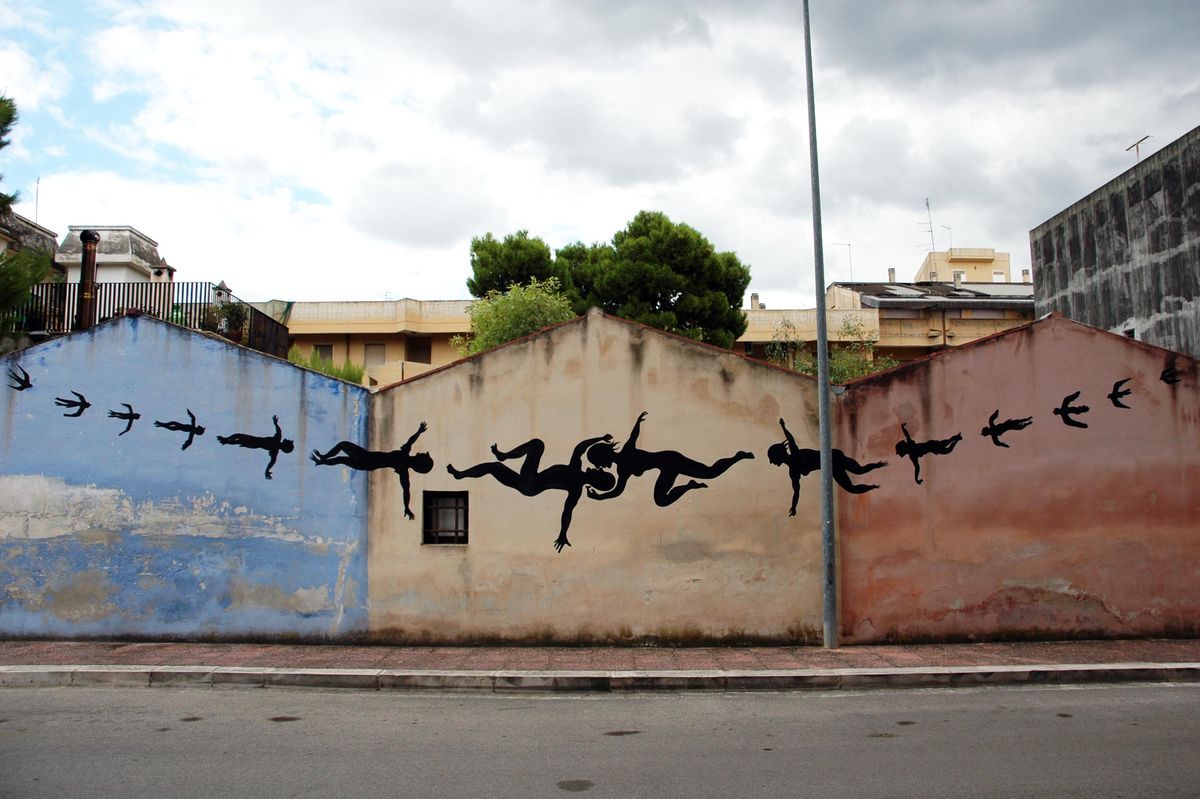 Row of black silhouette figures falling horizontally across three adjoining house gables painted blue, cream, and terracotta, flanked by flocks of small birds in flight, a street lamp post in front.