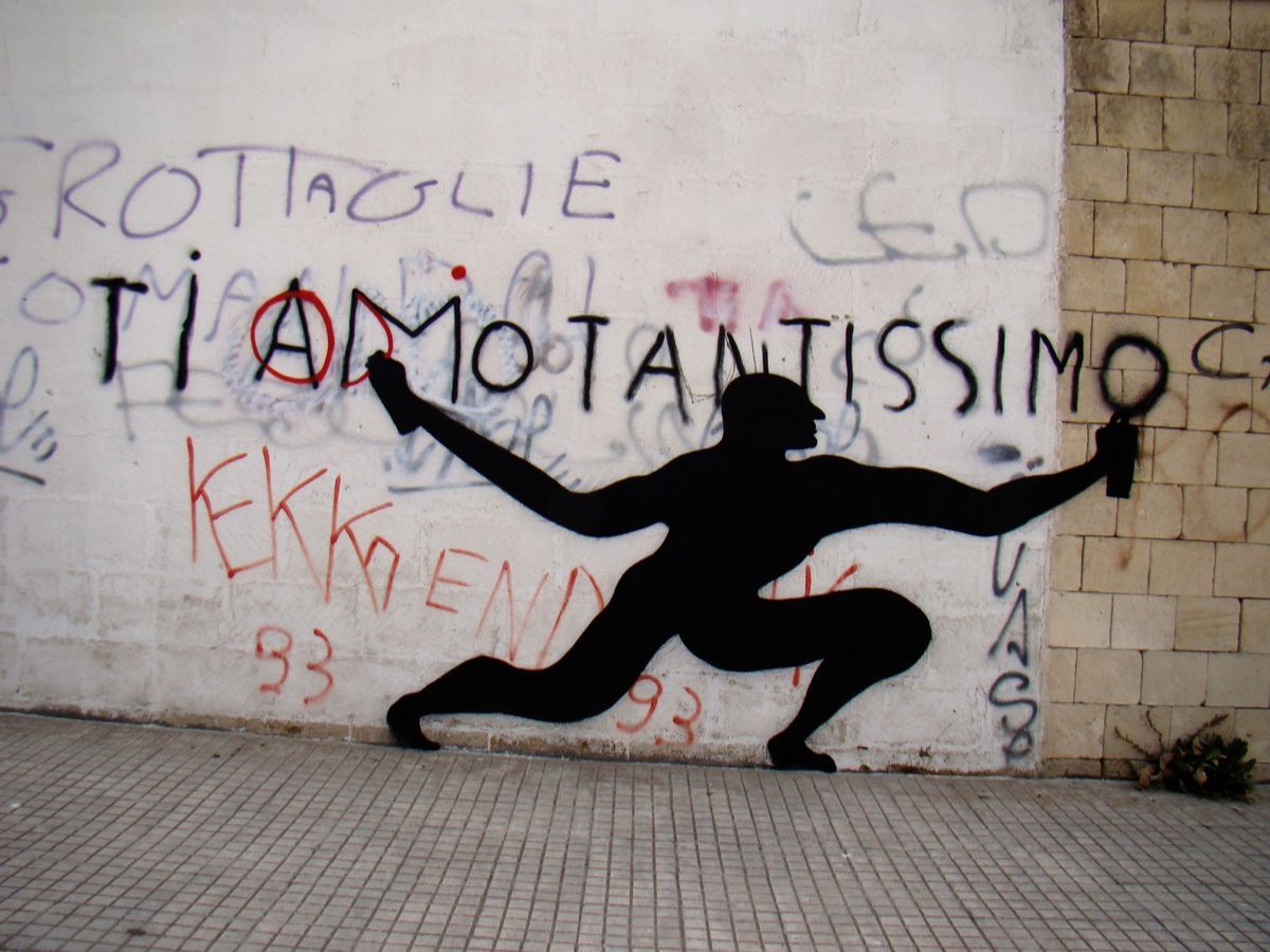 Black silhouette of a man in a lunging pose spray-painting the words TI AMO TANTISSIMO on a graffiti-covered stone wall, a spray can in each outstretched hand.